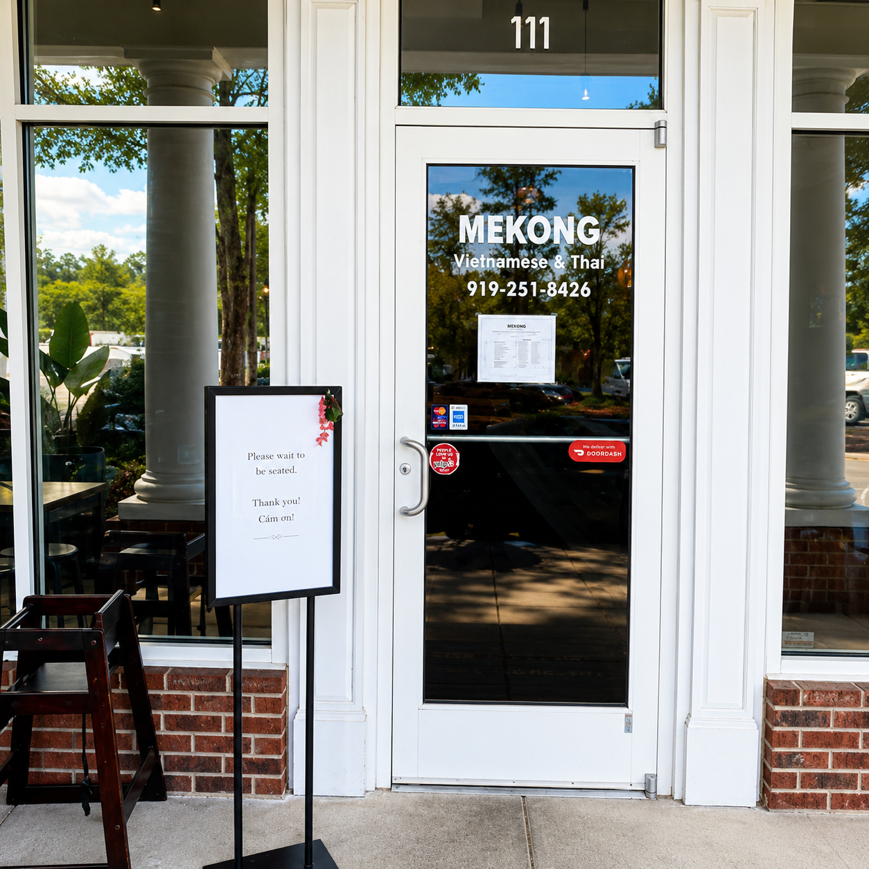 Front entrance door with restaurant lettering, address number above, and a welcome sign beside the entry.